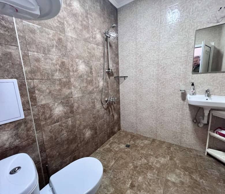 Bathroom with beige and brown tiles, shower, toilet, and sink in Magnolia Residence 5.
